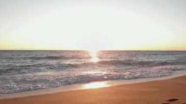 Deniz dalgaları gün batımında sahile vuruyor. Su yüzeyinde okyanus gün batımı