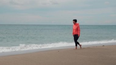 Kadın deniz sahilinde yürüyor, manzaranın ve doğanın tadını çıkarıyor. Özgürlük ve mutluluk