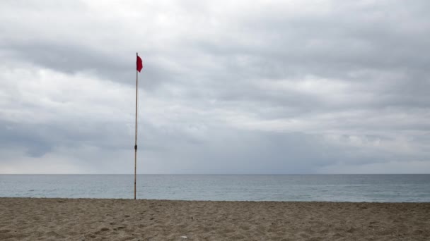 Fahnenmast mit Flagge der Türkei weht im Wind am leeren Strand vor grauem Himmel und stürmischer See — Stockvideo