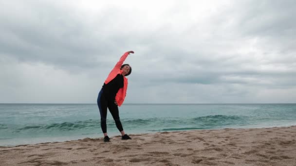 A mulher está a esticar-se na praia. Desportista está fazendo exercício de fitness ao ar livre — Vídeo de Stock