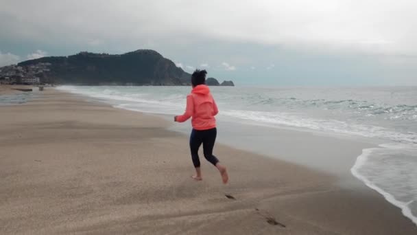 Samotna kobieta biega po pustej plaży. Kobieta biegnie wzdłuż burzliwego oceanu z dużymi falami — Wideo stockowe