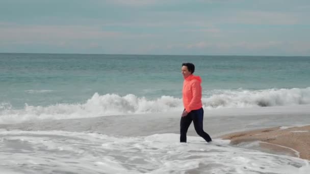 Feliz sorridente feminino está andando na praia tropical no dia ventoso tempestuoso — Vídeo de Stock