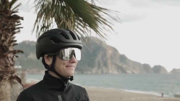 Женщина-велогонщица в профессиональных очках и черном шлеме против горного ландшафта — стоковое видео