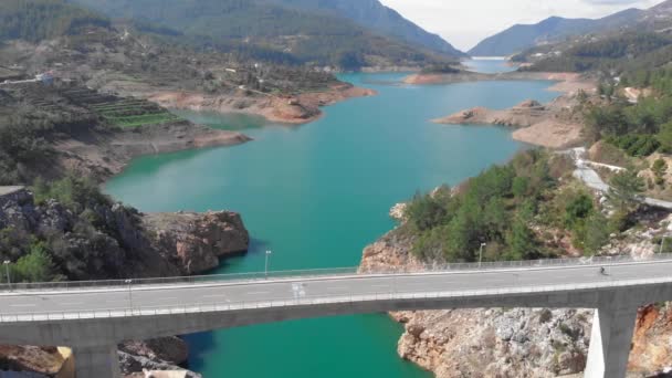 Beautiful clear azure lake with mountain cliffs, cyclist is riding on bicycle on bridge — Stock Video