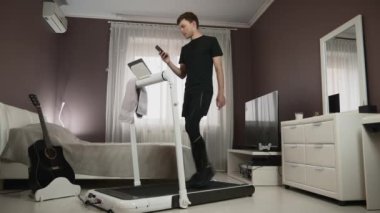 Adam koşu bandında antrenman yapıyor, akıllı telefondan internette yenisini izliyor. Sağlıklı yaşam tarzı