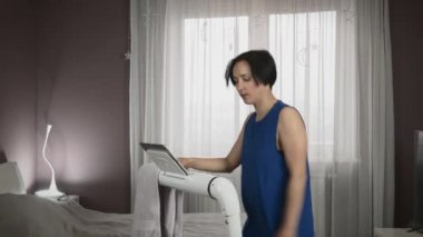 Tombul kadın evde koşu bandında koşuyor. Kadın çalışan makine üzerinde egzersiz yapıyor.