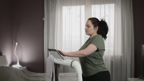 Frau läuft auf Laufband, berührt Tablet-Bildschirm, sieht Online-Fitnesstraining — Stockvideo