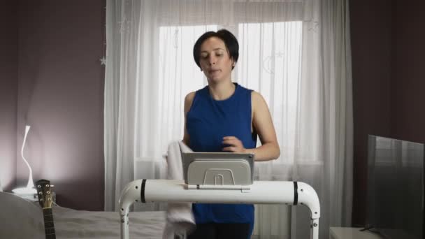한 여성 이 집에서 러닝 머신 위에서 뛰고 있고, 심장 운동을 열심히 하고, 인터넷에서 온라인 훈련을 보고 있습니다. — 비디오