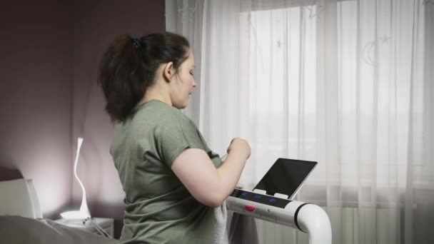 Frau trinkt Wasser beim Heimfitnesstraining auf Laufband im Wohnzimmer — Stockvideo