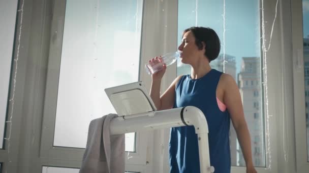 Junge Frau trinkt bei sonnigem Wetter Wasser aus Flasche beim Sport auf dem Laufband — Stockvideo