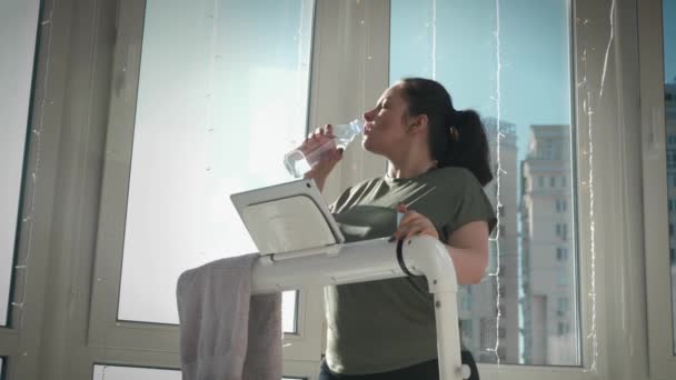 Frau trinkt Wasser aus Flasche, um beim intensiven Cardio-Training auf dem Laufband hydratisiert zu bleiben — Stockvideo