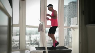 Koşu bandında egzersiz yaparken su içen bir adam. Erkek, akıllı antrenörde egzersiz yapar.