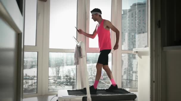 Comic man is exercising on treadmill, holding smartphone in hands, typing messages — Stock Video