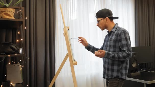 Man drawing picture. Artist working on painting, using brush, standing near easel — Vídeo de stock