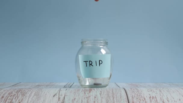 Saving money for trip. Putting coins into glass jar with inscription trip — Stock Video