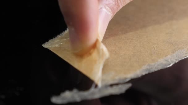 Közelkép a férfi ujjak lehámló le ragasztó papír fekete alapon — Stock videók
