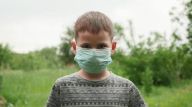 Koruyucu tıbbi maskeli çocuk kameraya bakıyor. Yüz maskesi takan çocuk