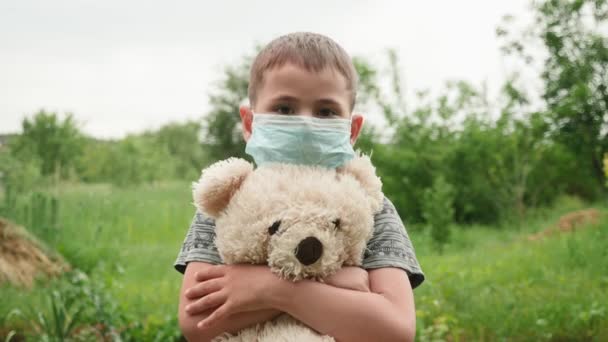 Bambino ragazzo in maschera medica protettiva guardando nella fotocamera e tenendo orsacchiotto — Video Stock