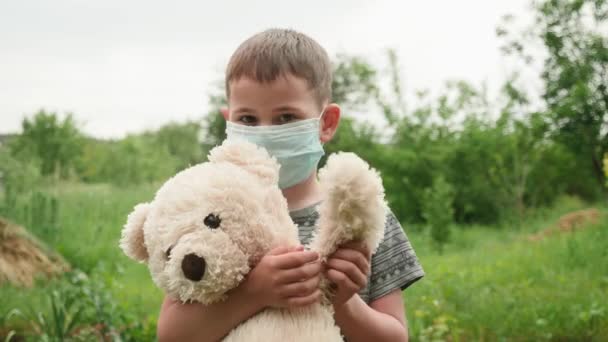 Ritratto di bambino carino in maschera blu protettiva con orso giocattolo in mano — Video Stock