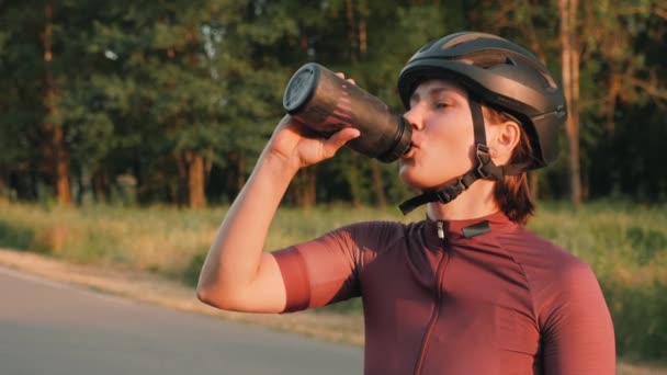 Велосипедист пьет воду во время велосипедных тренировок. Женщина пьет изотонические напитки, чтобы оставаться увлажненной на тяжелых тренировках — стоковое видео