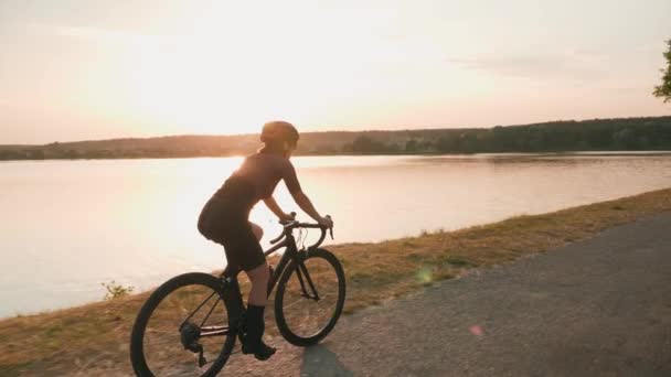 Woman cycling at sunset with sea on background. Cyclist riding on road bicycle at sunrise in sunlights — Stock Video