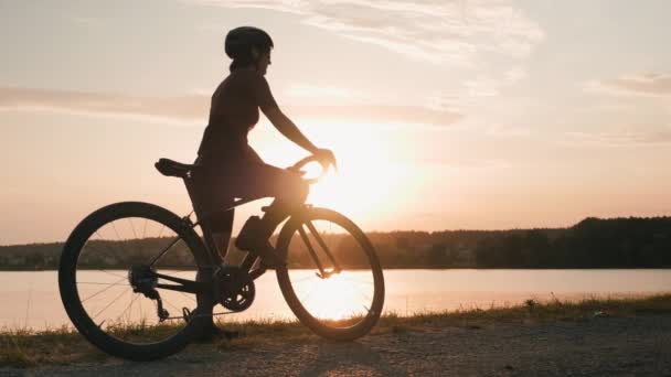 Woman cyclist at sunset. Professional cyclist starting to ride bicycle in evening sunshines — Stock Video