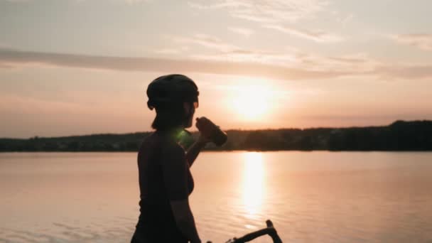 Gün batımında yoğun bisiklet eğitiminden sonra su içen bisikletçi kadın silueti. — Stok video