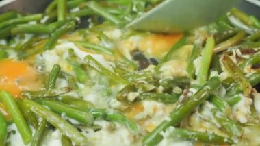 Stirring eggs and green beans in frying hot skillet. Frying eggs and green beans in pan