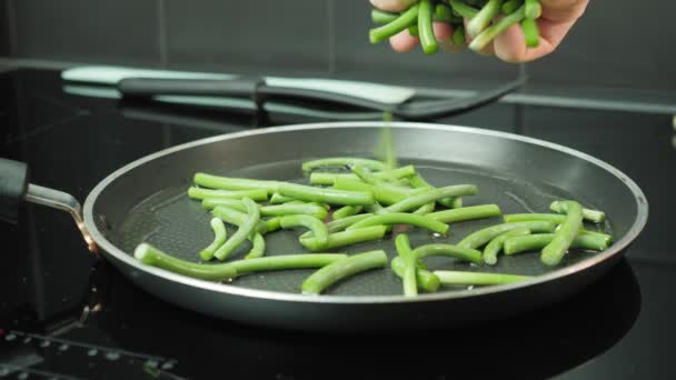 Die Hand des Mannes legt junge grüne Bohnen in die Pfanne. Chef bereitet Gericht mit Bohnen zu — Stockvideo