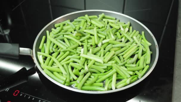 Preparing green beans on frying pan in modern kitchen. Cooking young sprouts of garlic in pan — Stock Video