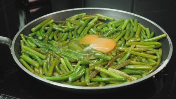 Quebrando ovos em frigideira com feijão verde frito. Preparação de alimentos saudáveis — Vídeo de Stock