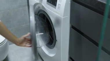 Çamaşır makinesinden çamaşırları çıkaran kadın. Eller kurutucudan temiz çamaşır alıyor.