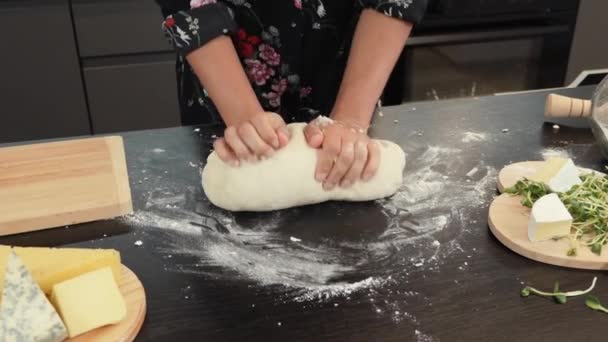 Female rolls and shapes dough in flour on workplace in kitchen. Woman kneading dough — Stock Video