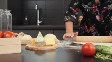 Kadın ahşap masada pizza için hamur yapıyor. Kadın hamuru oklavayla çeviriyor