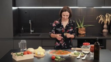 İtalyan pizza margherita 'sına fesleğen yaprağı ekliyorum. Kadın pizzaya yeşil fesleğen ekliyor