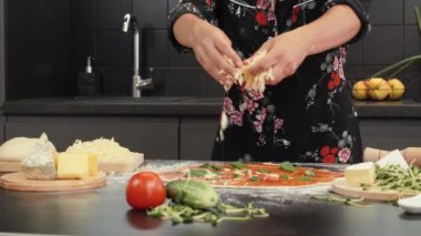 Tahta masada pizzaya peynir ekliyorum. Pizzanın üstüne peynir döken eller.