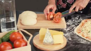 Kadın bıçakla domates doğruyor, ev yapımı pizza yapıyor. Eller bıçakla domates kesiyor.