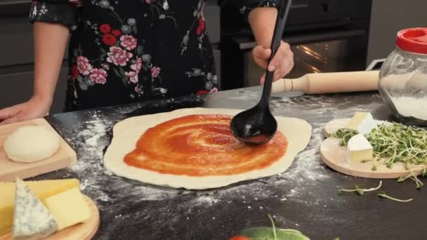 Esparciendo salsa de tomate en masa de pizza. Profesional mujer chef verter salsa en la pizza con cucharón — Vídeos de Stock