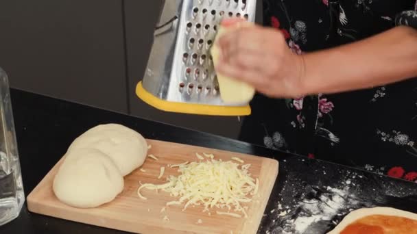 Grating cheese on wooden chopping board. Female hands grate hard cheese for pizza — Stock Video