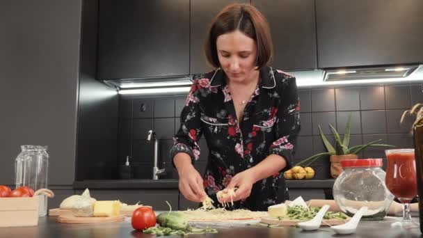 Femme pose fromage râpé sur la base de la pizza. Femme ajoutant du fromage à la pizza sur une table en bois — Video