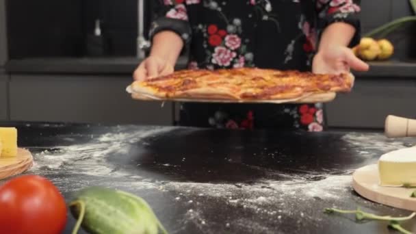 Вкусная запеченная пицца на деревянном столе. Женщина кладет приготовленную пиццу на стол на кухне — стоковое видео