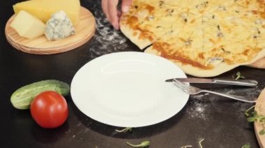 Kadın eli, peynirli pizzayı tabağa koyuyor. Masada nefis pişmiş pizza