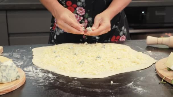 Händerna sätter blå dorblu ost på pizzabasen. Kvinnlig kock gör pizza i restaurangkök — Stockvideo