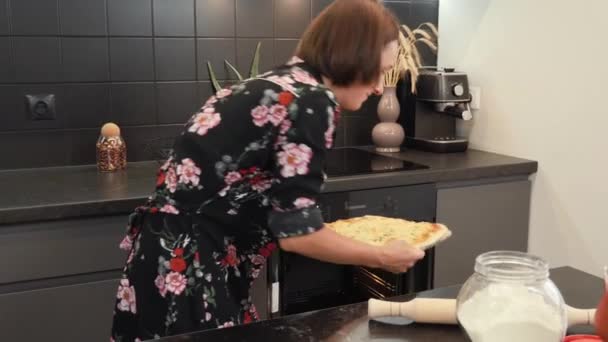 Femme sort pizza au fromage au four, met sur la table en bois et souriant à la caméra — Video
