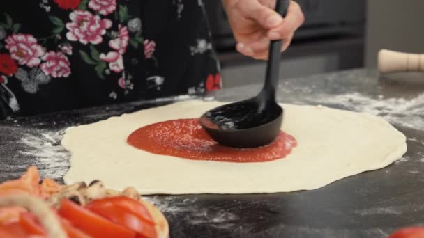 Menyebarkan saus tomat di dasar pizza. Koki wanita menuangkan saus di atas pizza dengan sendok — Stok Video