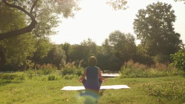 Mulher fazendo ioga ao ar livre no tapete. Feminino sentado em posição de lótus e meditando — Vídeo de Stock