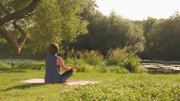 Woman meditating in park at sunrise. Female sitting in lotus position practicing yoga — Stock Video