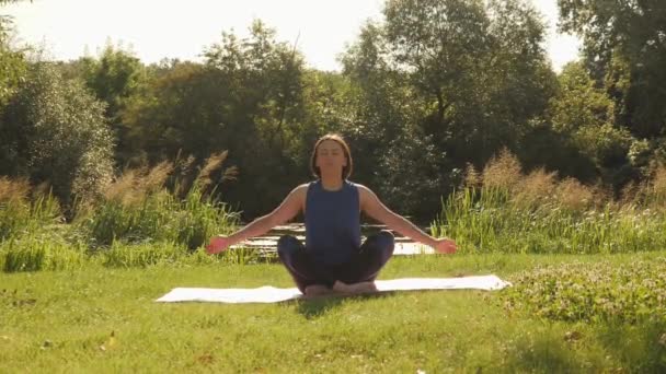 Practicar yoga al aire libre. Mujer realizando yoga frente al hermoso río en el parque de verano — Vídeo de stock