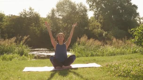 Mujer sentada en posición de loto sobre esterilla de yoga y sintiendo armonía de su cuerpo — Vídeos de Stock