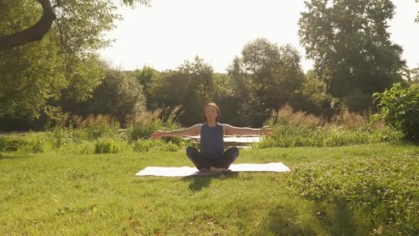 Jovencita haciendo ejercicios de yoga en el bosque. Mujer practicando yoga en el parque al amanecer — Vídeo de stock